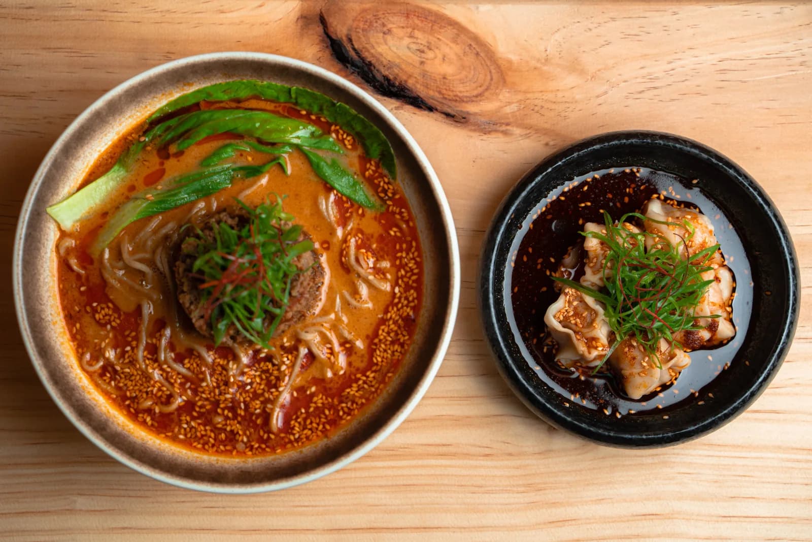 A bowl of tantanmen beside a side of gyoza on the wooden counter